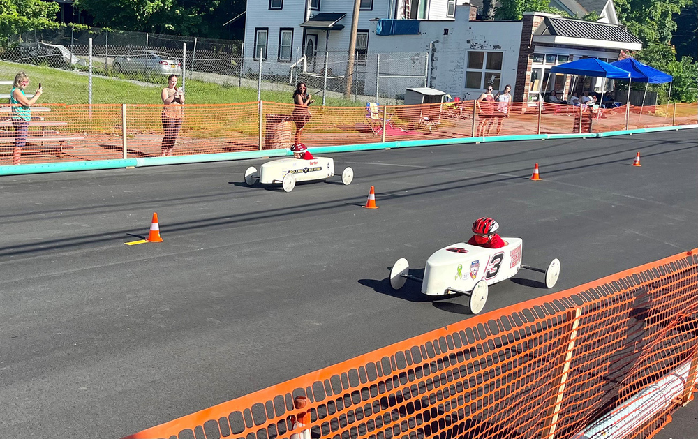 Two soap box derby cars race down the street