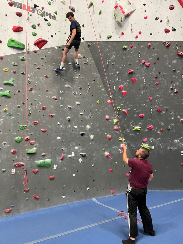 a student climbs a rock wall as a person belays