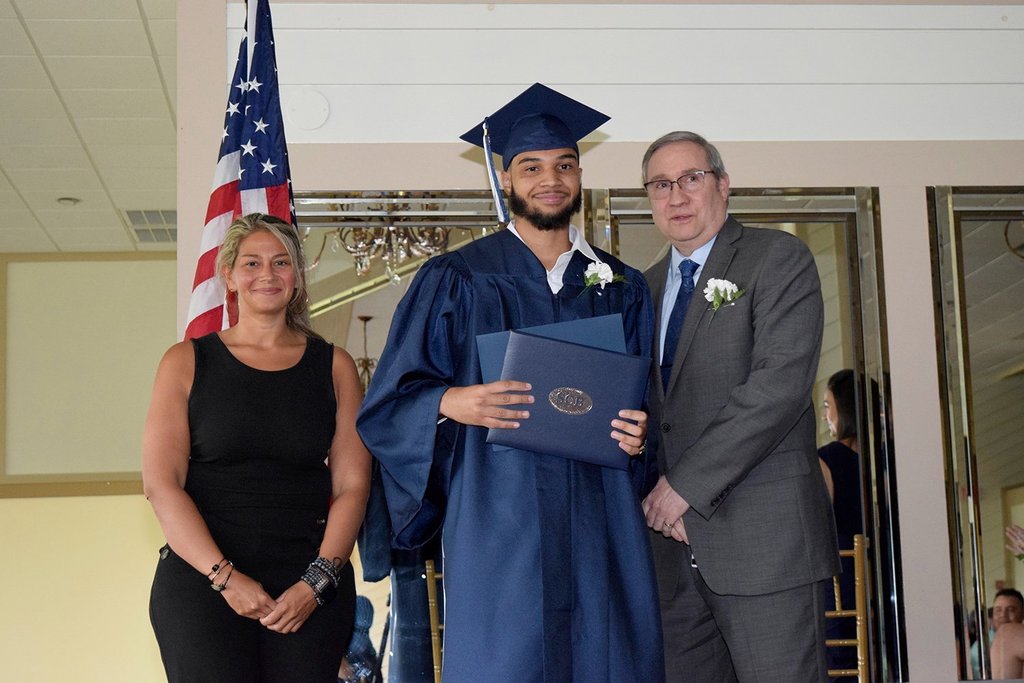 Christian Ramirez  stands between two people while holding a diploma