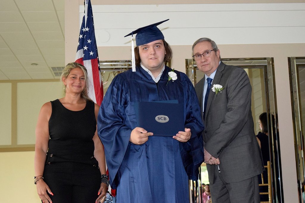 Avery Hund-Gately stands between two people while holding a diploma