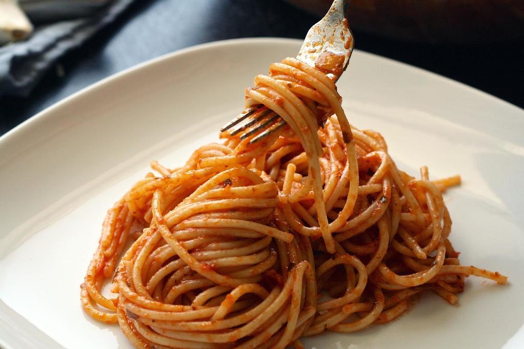 A fork holds spaghetti covered in sauce up from a round white plate