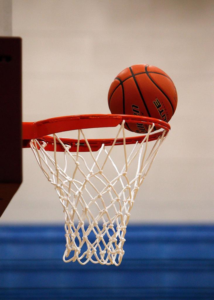 A basketball sits on the rim of a basketball hoop shown from the side