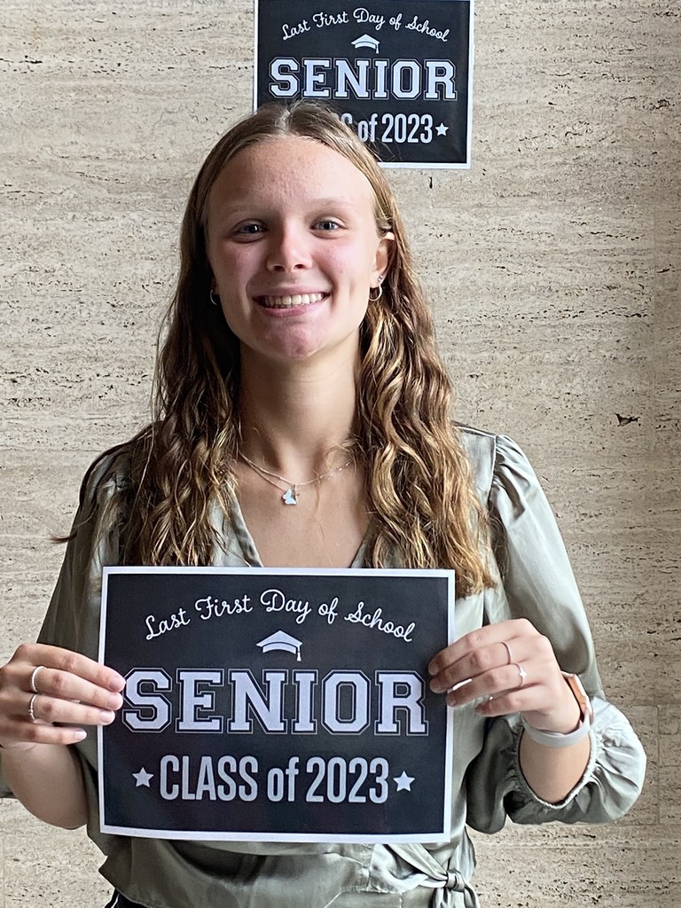 A student in a green patterned shirt holds a black sign with white letters that reads "Last first day of school Seniors Class of 2023"