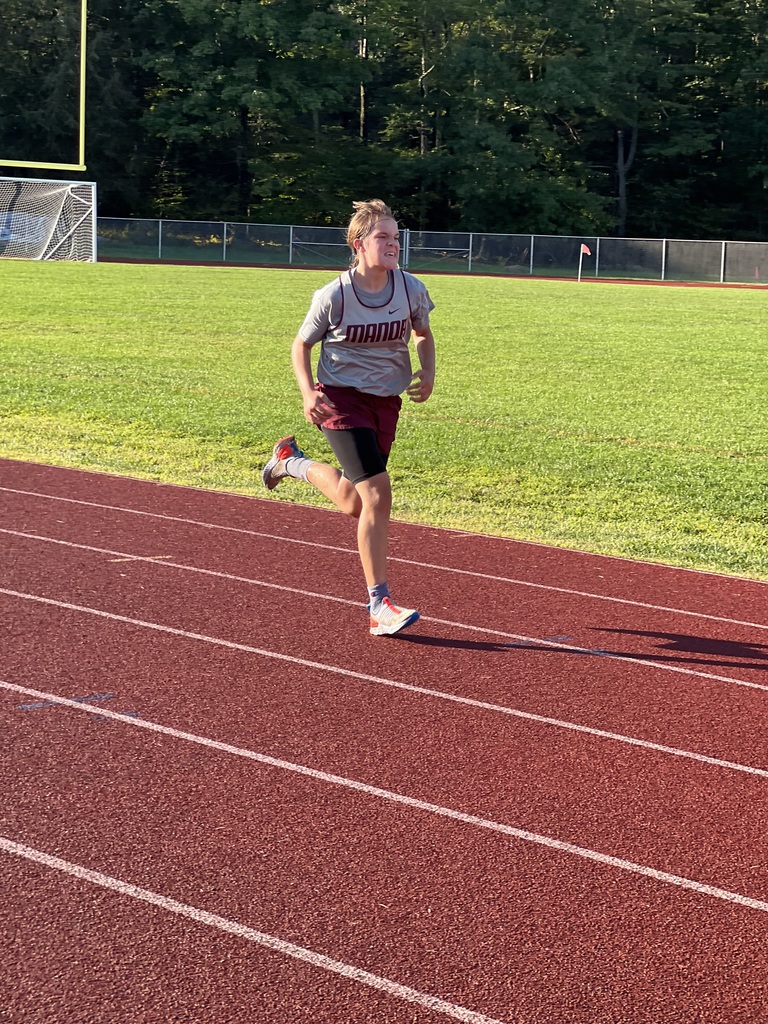 A runner in a gray and maroon uniform runs on a maroon track with green grass in the background.
