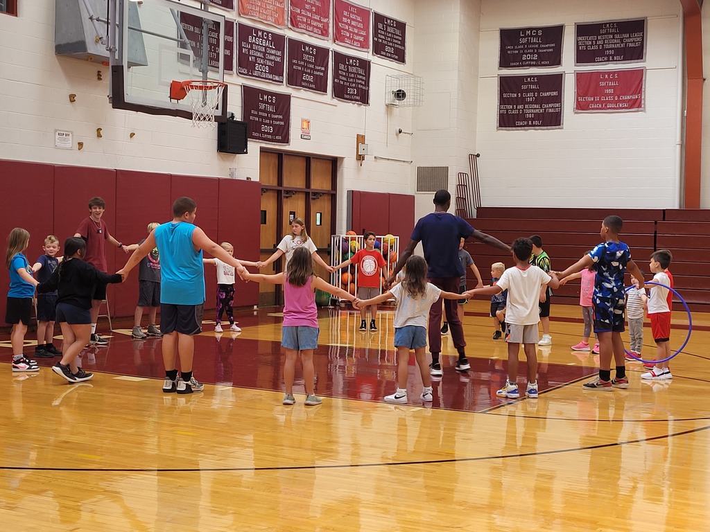 Students stand in a gymnasium in a circle holding hands with an instructor in the middle 