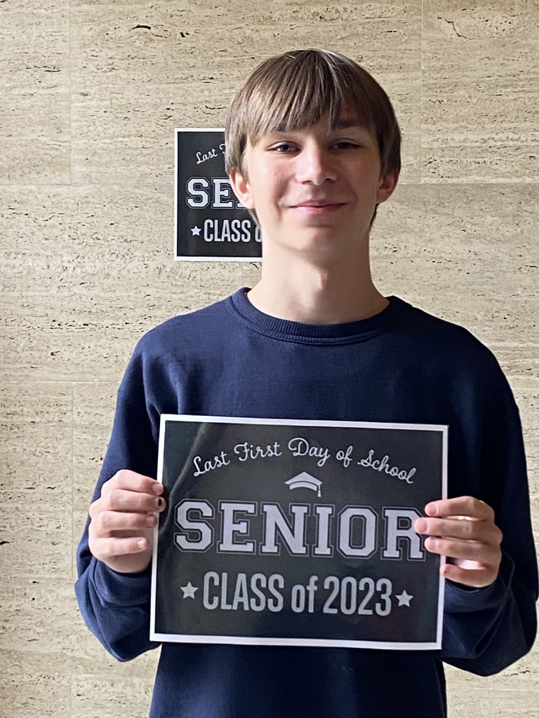 A student in a black shirt holds a black sign with white letters that reads "Last first day of school Seniors Class of 2023"