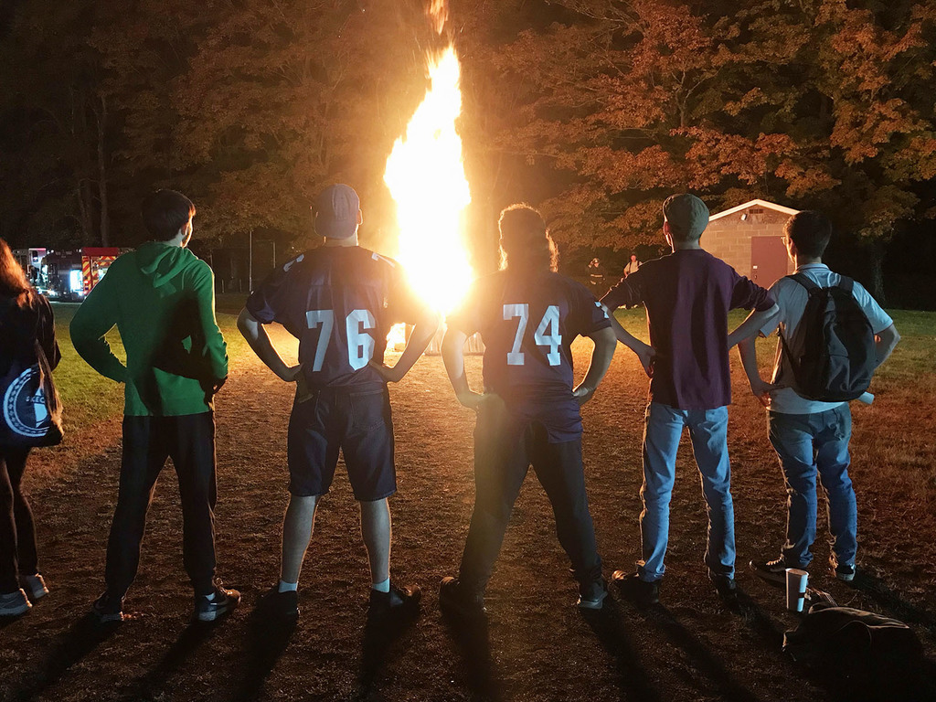 Five people are seen with their back to the camera facing a bonfire