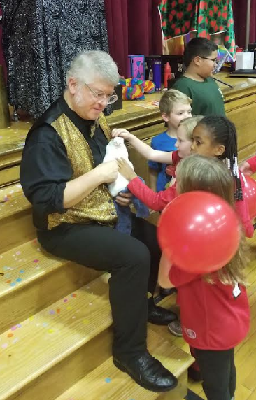 A magician sits on stars and shows a trick to  students.