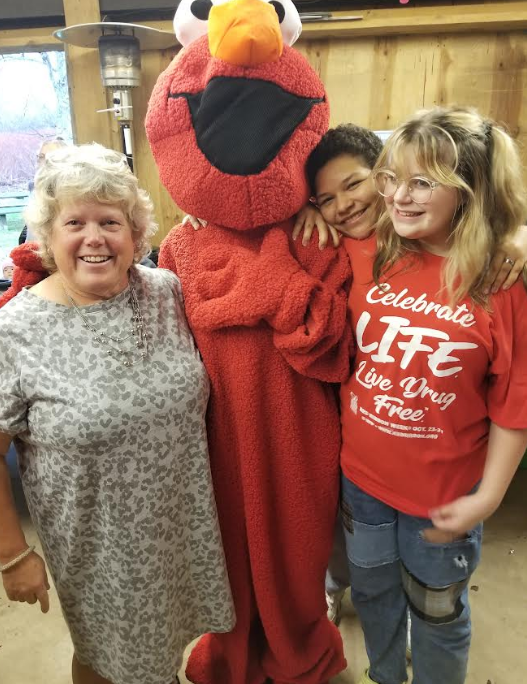 Three people pose with an Elmo costumed person