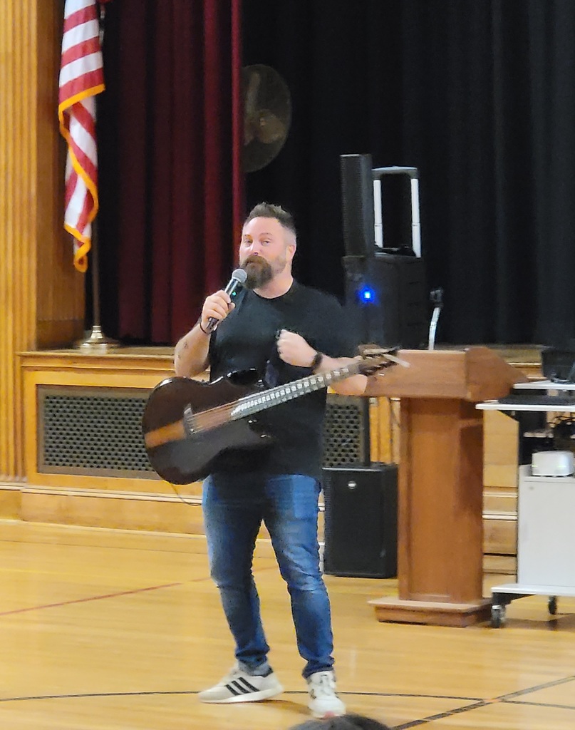 A man speaks into a microphone while holding a guitar