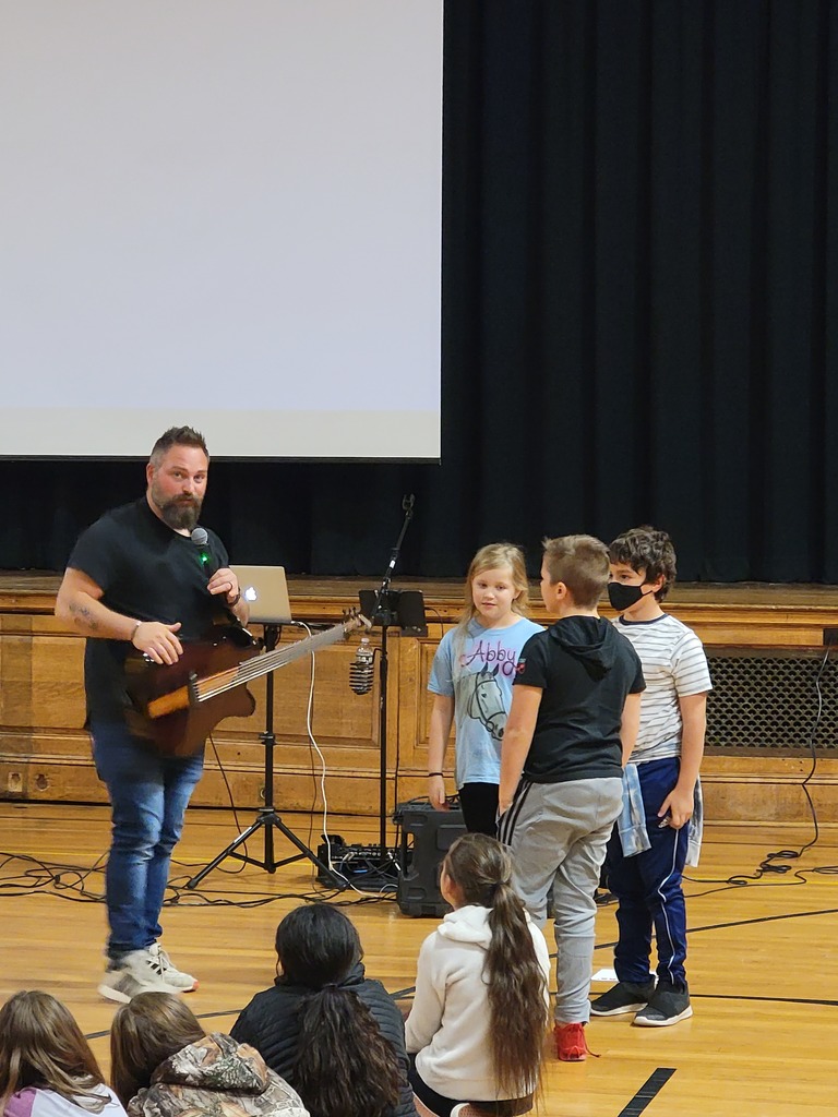 A man holding a guitar speaks to three students