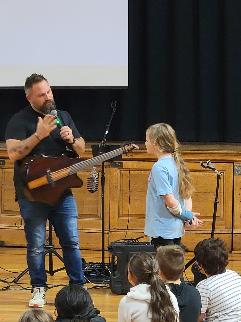 a man holding a guitar and a microphone speaks to a student