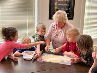 A teacher helps younger students cut out cookies