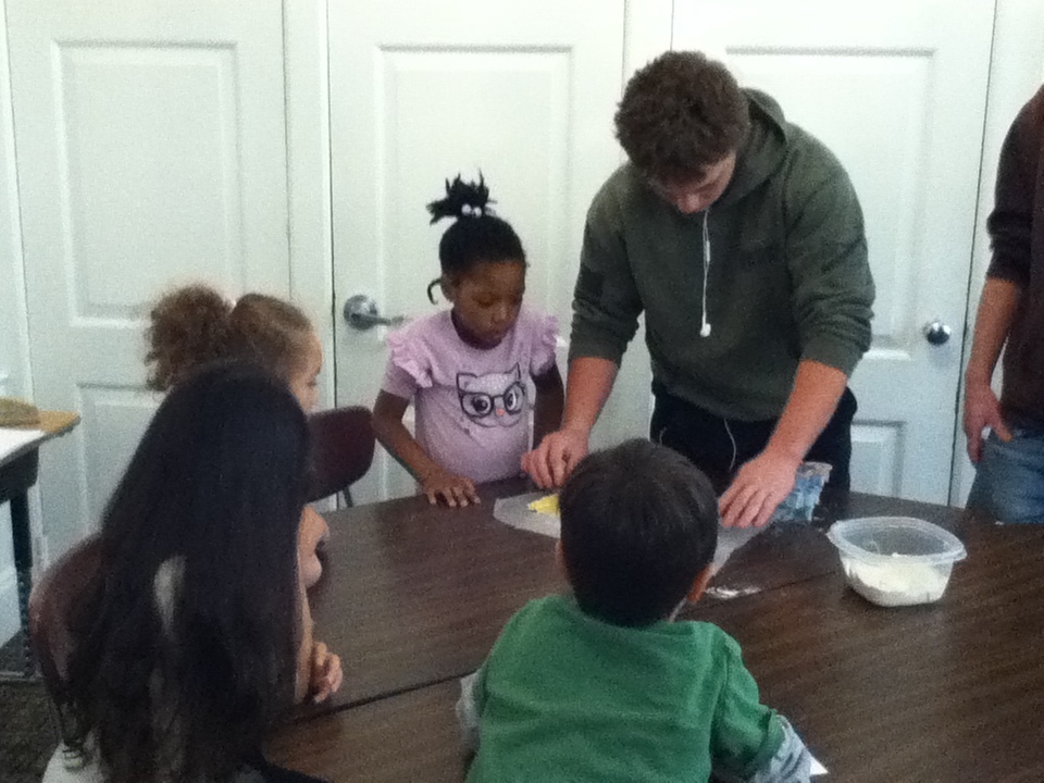 An older student works with a group of younger students making cookies.