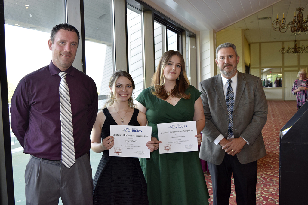 Two students hold certificates as two administrators flank them