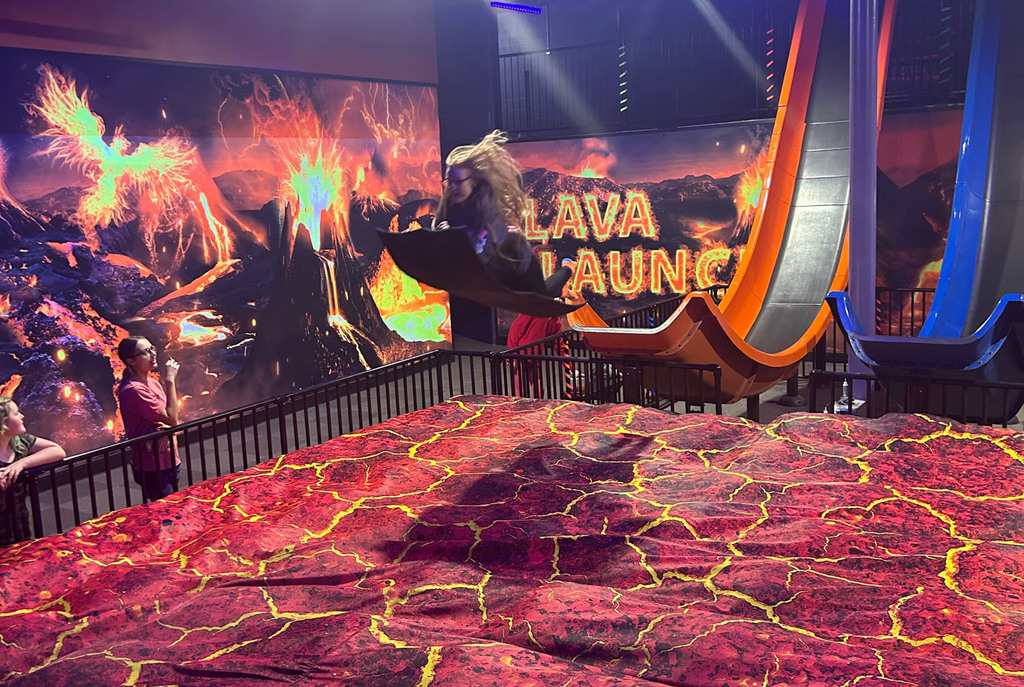 A student sails off the end of a slide into a mat made to look like lava.
