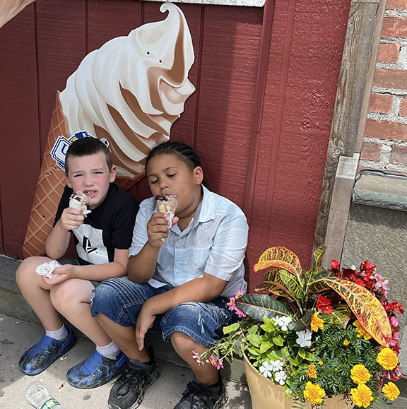 Two students eat ice cream in front of an icecream shaped sign