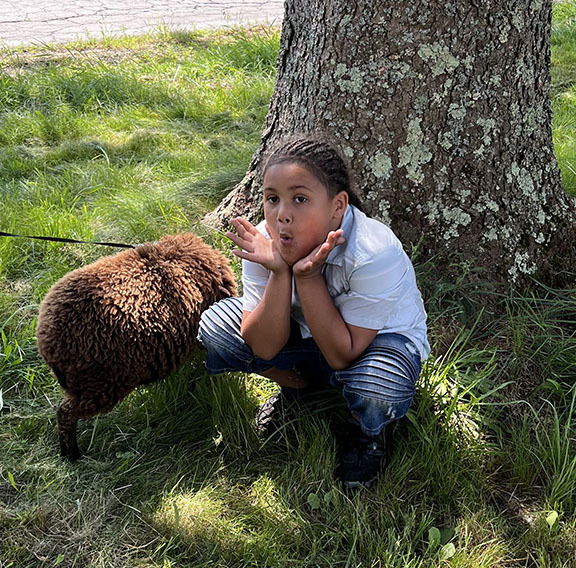 A student makes a funny face crouching next to a brown lamb