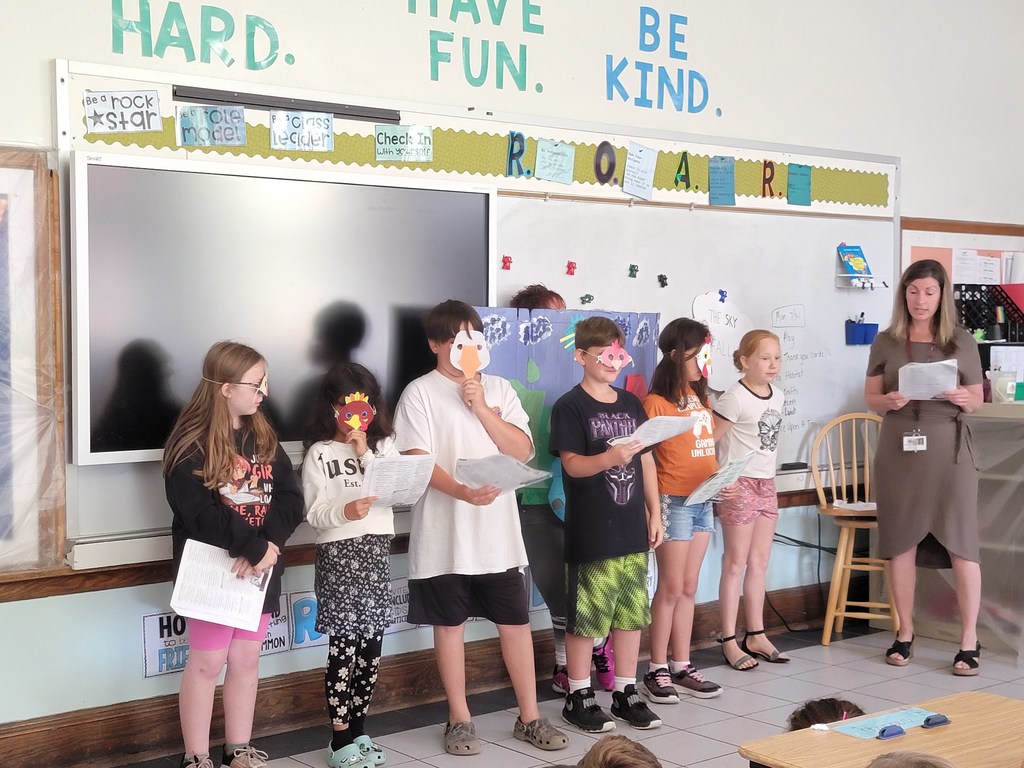 Bird-mask wearing students under the direction of an adult perform a reading of a play