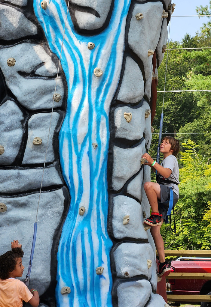 A student climbs the side of a rock climbing wall painted like rocks and a stream.