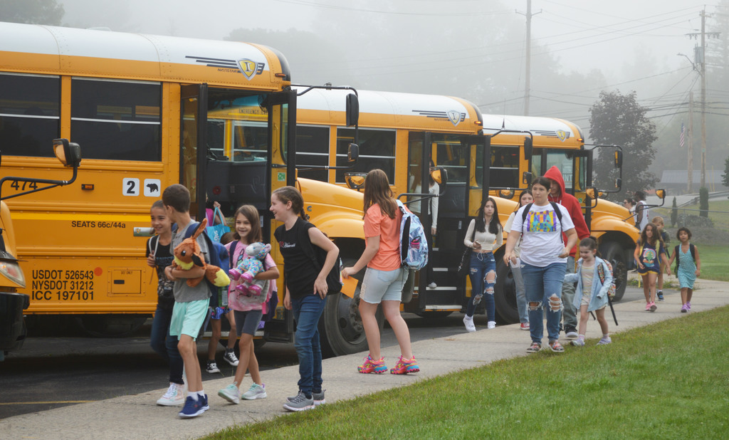 Students depart buses and walk up a sidewalk