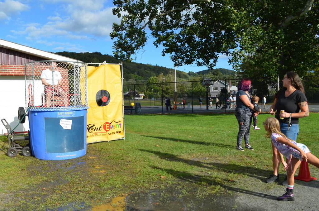 A student throws a ball at a target on a dunk tank that a man is sitting in as other people stand in the background