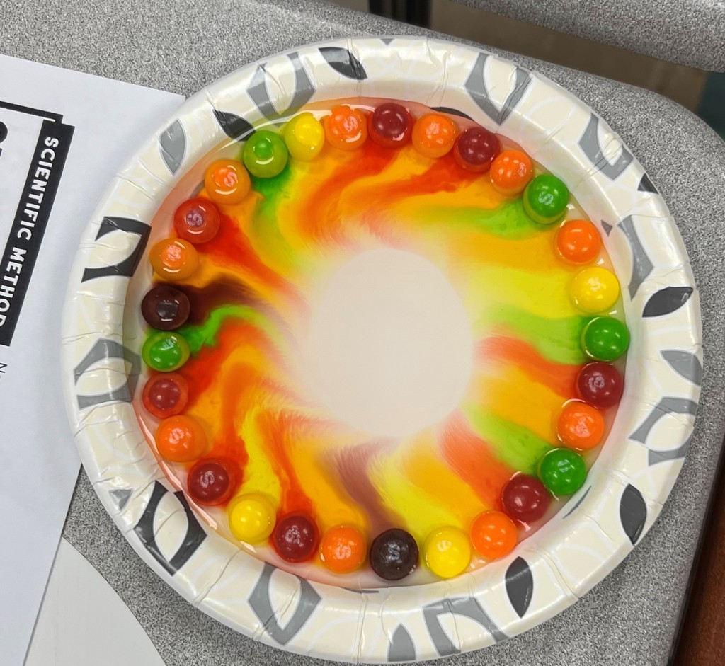Color drains from Skittles covered with water without colors mixing on a plate