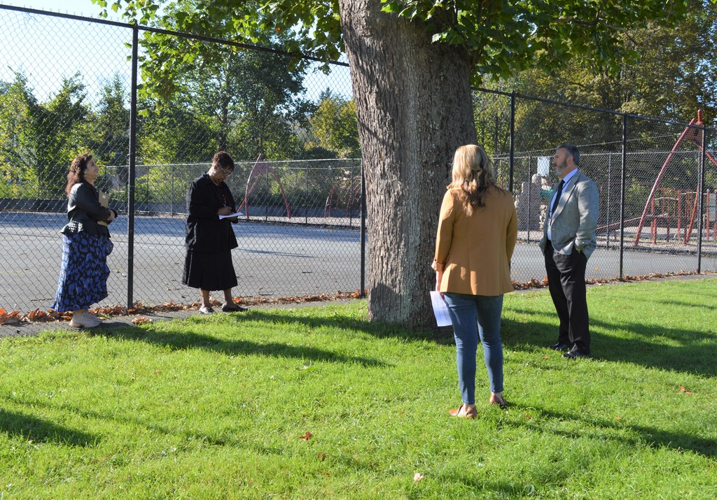 Four people stand near a blacktop courts and a large tree