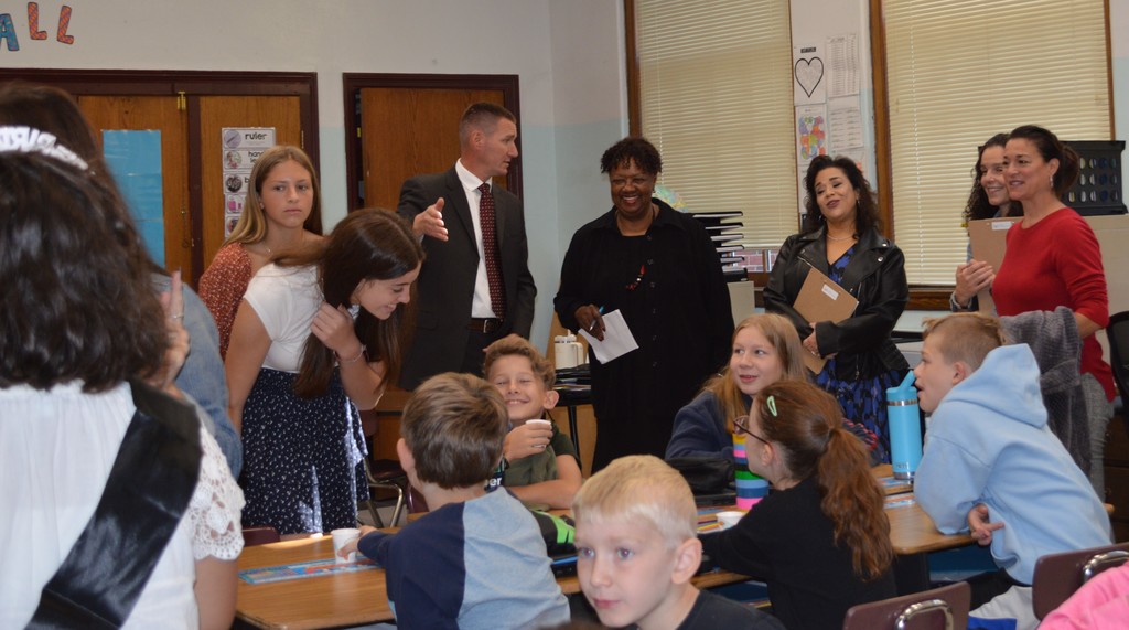 adults stand at the back of a classroom a students sit at desks