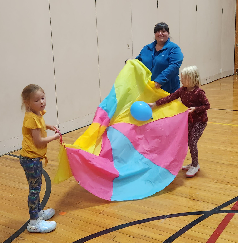 Two young students and an adult play with a parachute  and a balloon