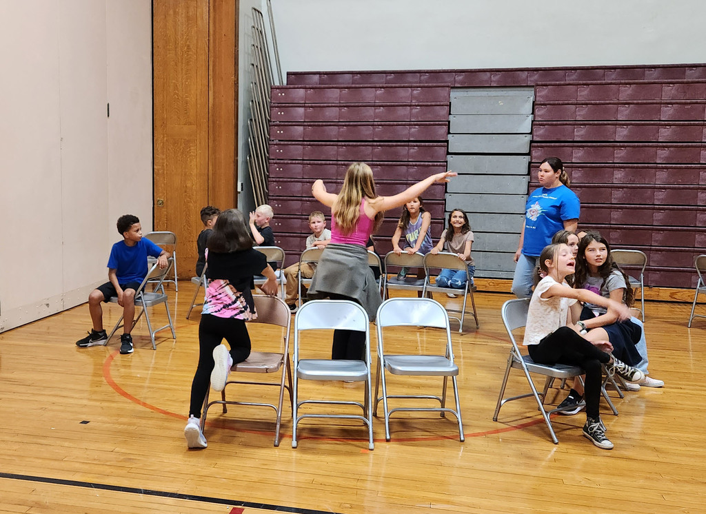 Folding chairs face out in a circle as student watch an older student in the middle